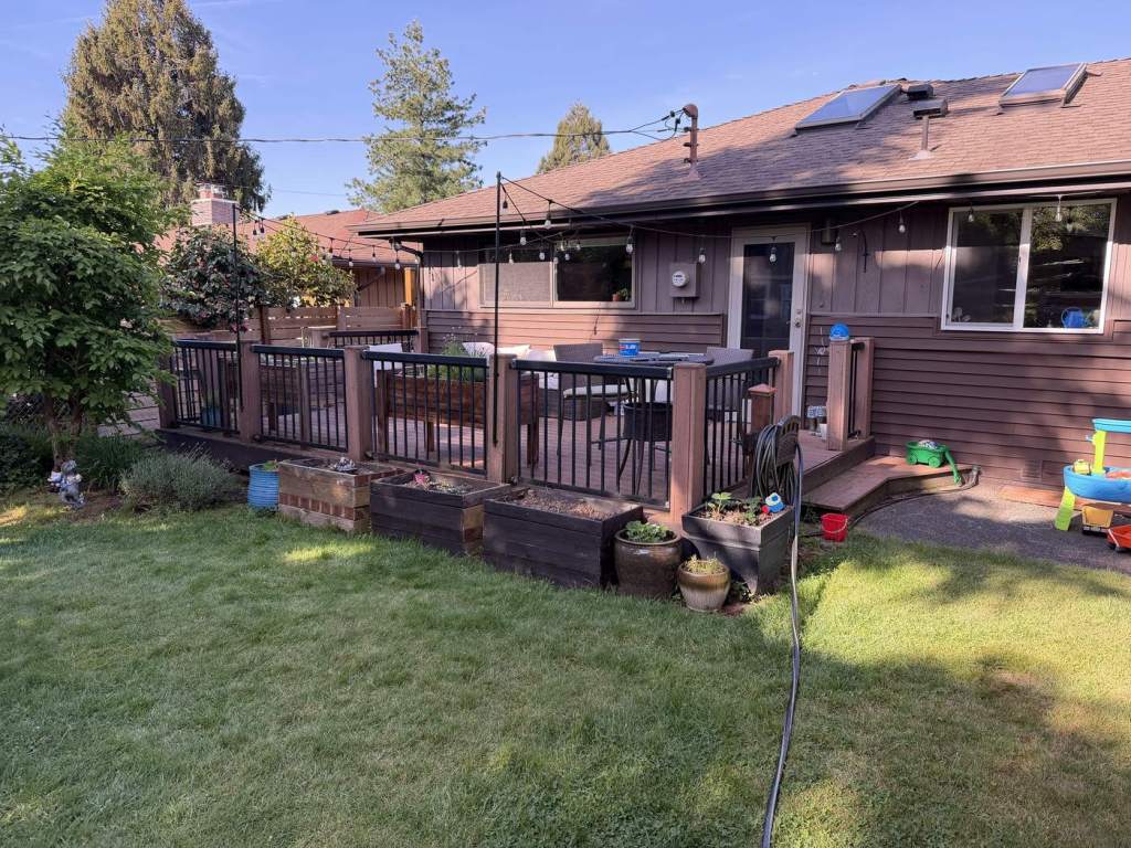 The original wood deck seen from the lawn, with timber posts and a metal picket railing.