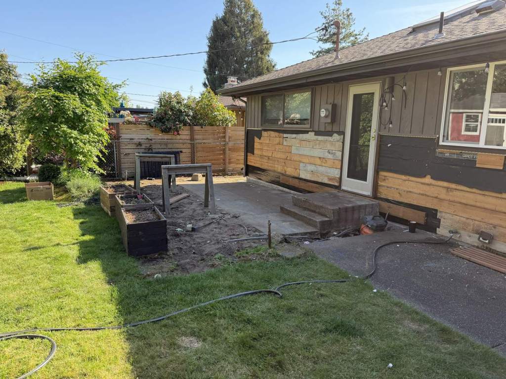The deck removed, leaving a bare concrete patio slab, with the siding opened up behind it.