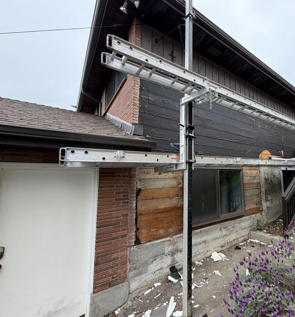 The side elevation stripped back to bare sheathing and building paper, with staging poles in place.