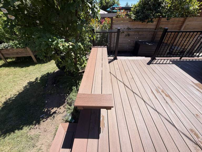 The finished deck with the built-in bench running along two sides and black metal railing behind.