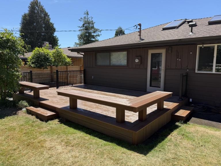 A finished composite deck with a built-in bench and metal railing at the back of a single-storey house.