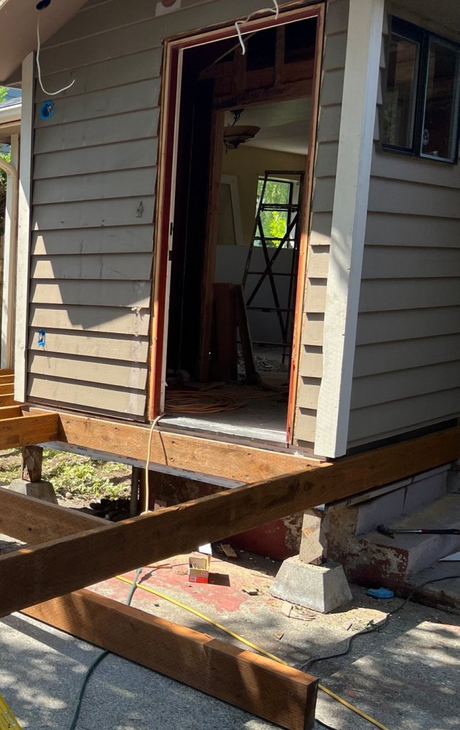 New deck framing at the door threshold, carried on posts and precast pier blocks.