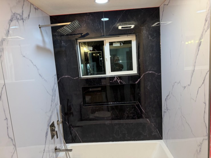 The finished Burien bathroom shower, black-and-white marble-look luxury vinyl paneling and a rain shower head