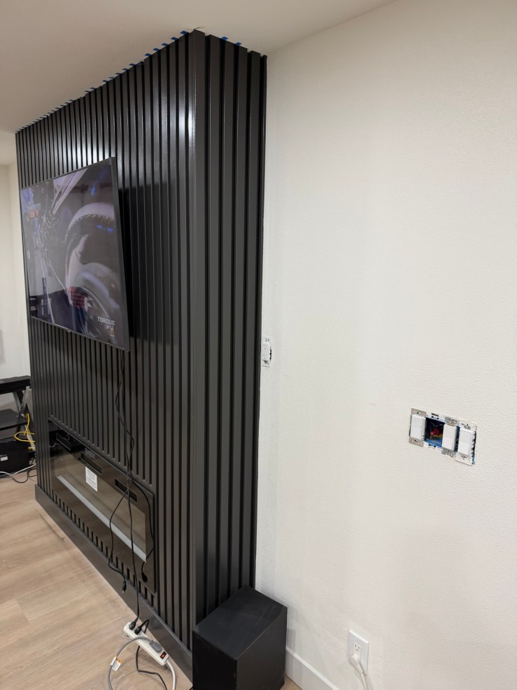 The new fluted black fireplace wall with a mounted TV in the Burien great room, opened up after removing a load-bearing wall and adding a structural beam