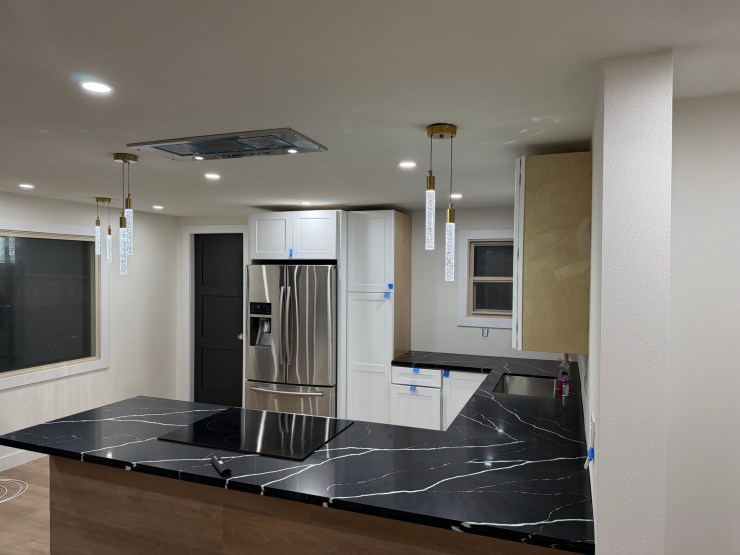 The finished Burien kitchen open to the living room, with a black waterfall island, white cabinetry, stainless appliances and the new fireplace wall beyond