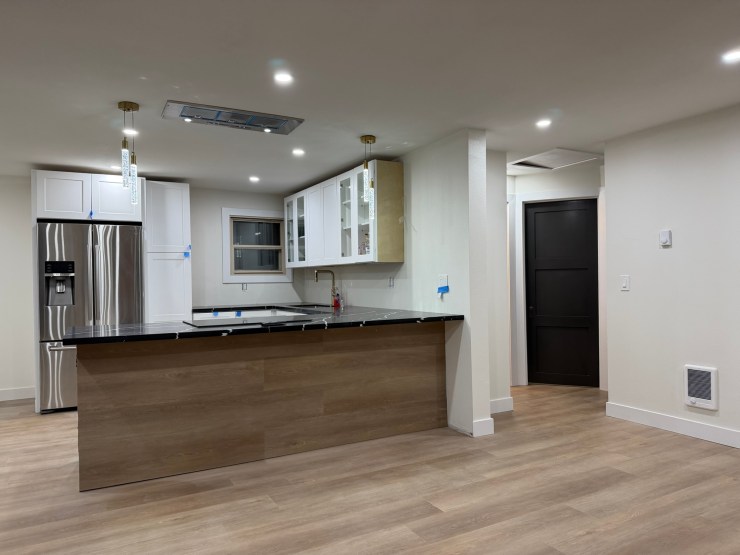 Wide view of the finished Burien kitchen and open living space, white cabinets and a black waterfall island