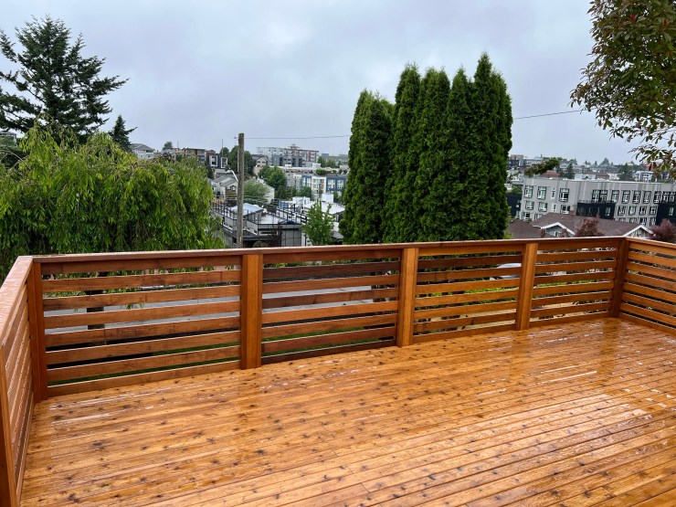 The finished West Seattle deck, freshly stained, with a horizontal cedar slat railing and a view over the neighborhood