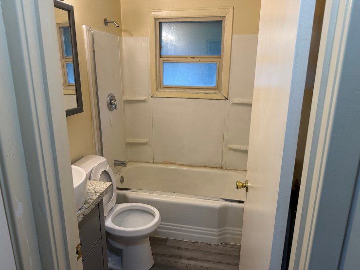The original Burien bathroom before the remodel, dated yellowed tile and a standard tub-shower